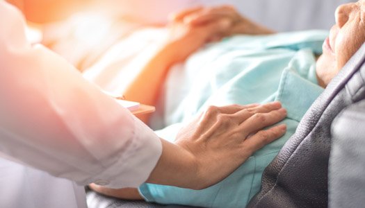 Healthcare provider placing their hand on a patient lying in bed