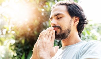 Man in a Yoga pose with sun shining in the background