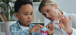a boy stacking blocks next to a woman evaluating him