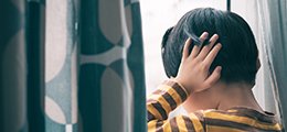 Young boy covering his ears looking out of a window