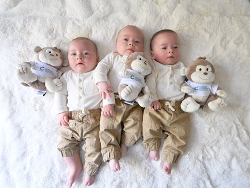 3 babies laying on a bed with teddy bears