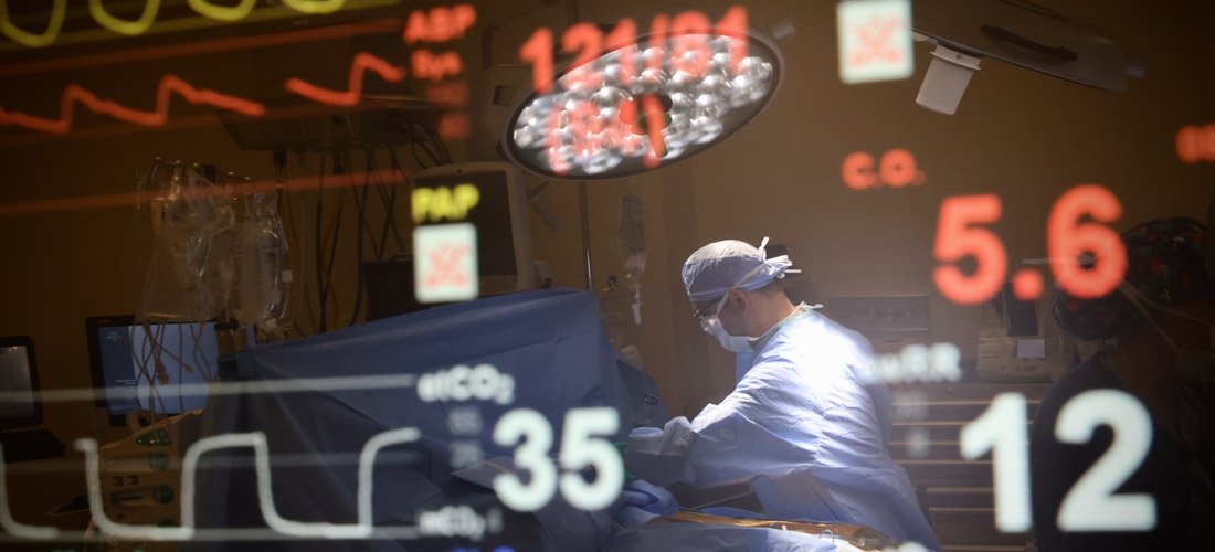 Heart monitor in a surgical room with a reflection of a surgeon performing a procedure