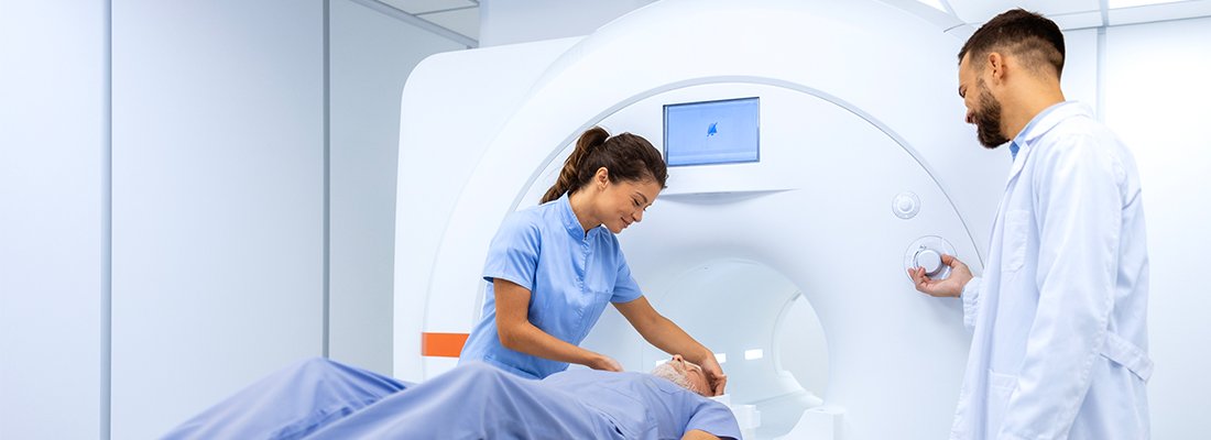 radiologists processing an elder male patient into a large imaging machine