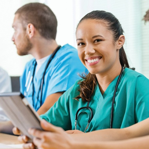 A female nursing student smiling and taking notes at a table with other students