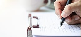 a hand holding a pen, filling out papers on a clipboard