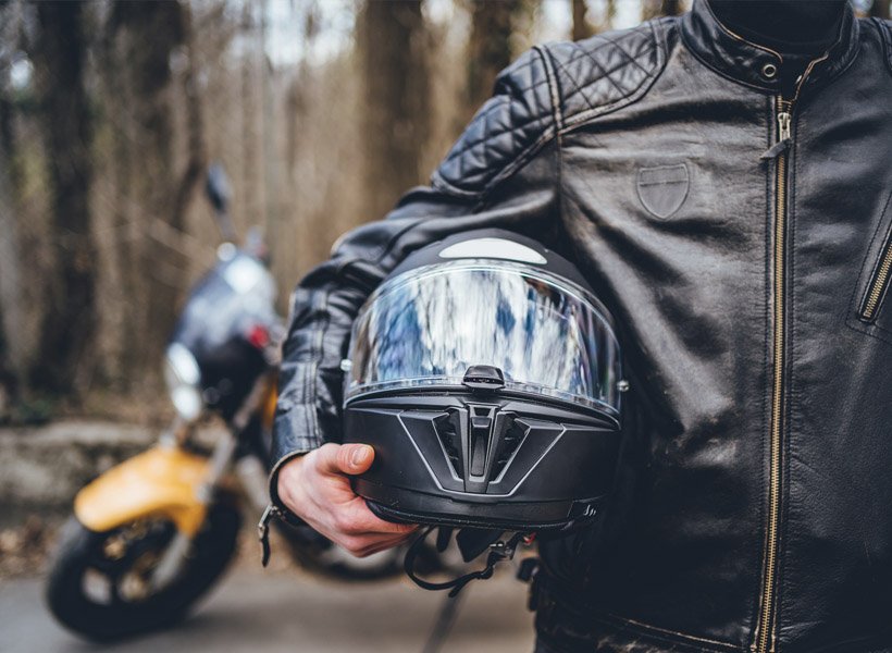 Motorcyclist holding a helmet and standing in front of their motorcycle