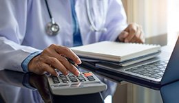 A clinical professional sitting at a laptop with a calculator