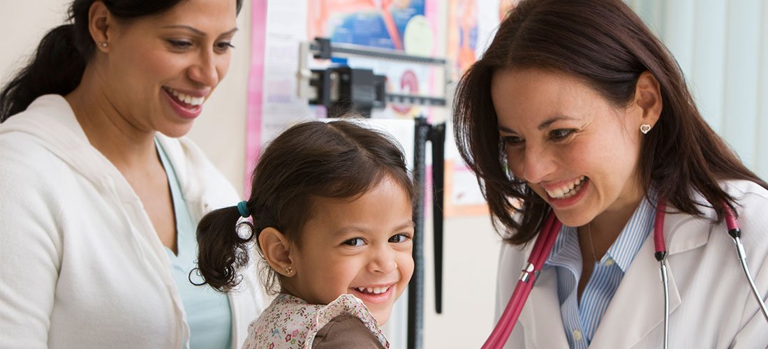 A mother stands near her daughter as a pediatrician checks the girl